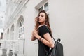 Modern young woman in black fashionable clothes straightens hair. Attractive joyful girl model in a black dress with a backpack Royalty Free Stock Photo