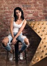 Modern young woman posing on a chair. Stylish appearance, white t-shirt and jeans with holes Royalty Free Stock Photo