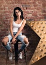 Modern young woman posing on a chair. Stylish appearance, white t-shirt and jeans with holes