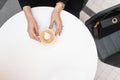 Modern young woman sits at a vintage white table in a cafe and holds  a cup of hot delicious cappuccino. Top view on the table Royalty Free Stock Photo