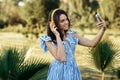 Modern young woman in summer dress listening to music with headphones and take selfie on smartphone outdoor. Royalty Free Stock Photo