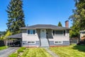 Modest residential house with car parked under the canopy on asphalt driveway. Family house with freshley mowed lawn on the yard