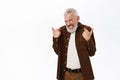 Modest senior guy, man with grey hair pointing fingers at himself with shy smily, standing over white background