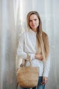 Modest woman in white sunlit room posing for a photo, holding wicker bag Royalty Free Stock Photo