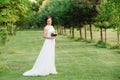 A modest young girl in a nice wedding dress stands alone in a green garden Royalty Free Stock Photo