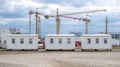 Modular office units standing aligned at construction site, industrial cranes operating beneath overcast sky with neutral lighting Royalty Free Stock Photo