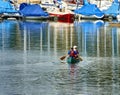 Two older men with life jackets paddle in a canoe on the lake near the pier with moored sailboats