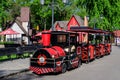 Mogosoaia, Romania - 7 May 2021: Vivid red train for children in front of colourful wooden houses in Mogosoaia Park in a sunny