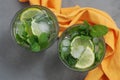 Mohito Alcohol Drink. Two Glasses with Cocktail Drinks and Ice cubes and limes citrus fruits.