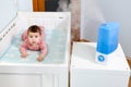 Moistening of air in children room for prevention pulmonary disease, baby girl lying in crib with humidifier in use next to her Royalty Free Stock Photo