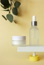 Moisturizer cream and serum in bottle standing on abstract pedestal on pastel yellow background with copy space