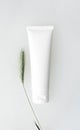 Moisturizer cream, shampoo or facial cleanser in white tube mockup and green spikelet on white water surface. Blank eco natural