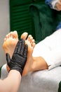 Moisturizing the feet. Hands of pedicure master in black gloves care about female feet. Foot massage. Pedicure beauty Royalty Free Stock Photo