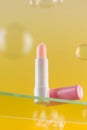 Moisturizing pink hygienic lipstick on a glass shelf on a yellow background with soap bubbles.