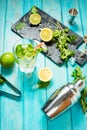 Mojito cocktail with lime and mint in highball glass on a blue wood table. Drink making tools and ingredients for cocktail