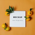 Mokeup spiral notebook with mandarines around, close up over orange background Royalty Free Stock Photo