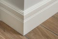 Molding in the interior, baseboard corner. Light matte wall with tiles immitating hardwood flooring Royalty Free Stock Photo