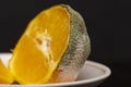 Moldy orange lies on a plate, cut in half on a dark background, texture of green mold, selective focus. Not fresh, but rotten frui