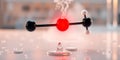 Molecular structure with red central atom and black, white outer atoms releasing vapor against a blurred background Royalty Free Stock Photo