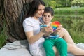 Mom and baby boy 4 years old play with a colored trendy toy Pop it in the park in nature. Antistress sensitive toy or