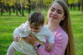 Mom with baby in bright clothes on a pink plaid on the green right. Family resting in the park on a warm day