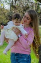 Mom with baby in bright clothes on a pink plaid on the green right. Family resting in the park on a warm day