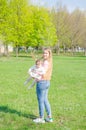 Mom with baby in bright clothes on a pink plaid on the green right. Family resting in the park on a warm day