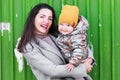 Mom with a baby on a green background. In a warm gray coat. Portrait of a beautiful girl with her son on a green background. Holds Royalty Free Stock Photo