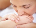 Mom, baby and kiss feet of child for love, care and relax in nursery room at home. Face, mother and closeup of foot of