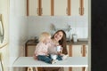 Mom and baby in kitchen. Young mom and toddler have breakfast at home