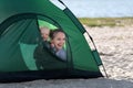 Mom and baby peeking out of tourist tent. Tent on the sandy beach. Camping
