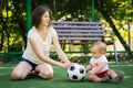 Mom and baby roll soccer ball to each other sitting at football field. Mother and son playing together. Summer family fun outdoors Royalty Free Stock Photo