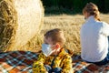 Mom and baby sit on the ground on the background of haystacks in medical masks Royalty Free Stock Photo