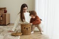 Mom and baby toddler pull toys out of basket. Babysitter and kid playing in room on floor