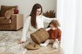 Mom and baby toddler pull toys out of basket. Babysitter and kid playing in room on floor