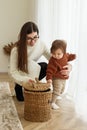 Mom and baby toddler pull toys out of basket. Babysitter and kid playing in room on floor