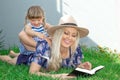 Mom blonde in a hat and her daughter are lying on the grass and reading a book, happy family. Royalty Free Stock Photo