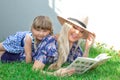 Mom blonde in a hat and her daughter are lying on the grass and reading a book, happy family. Royalty Free Stock Photo