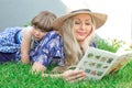 Mom blonde in a hat and her daughter are lying on the grass and reading a book, happy family. Royalty Free Stock Photo