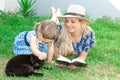 Mom blonde in a hat and her daughter are lying on the grass and reading a book, happy family. Royalty Free Stock Photo