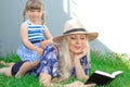 Mom blonde in a hat and her daughter are lying on the grass and reading a book, happy family. Royalty Free Stock Photo