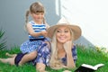 Mom blonde in a hat and her daughter are lying on the grass and reading a book, happy family. Royalty Free Stock Photo