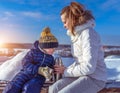 Mom with a boy son 3 years old, in the winter in a pair in the fresh air. Rest at the weekend resort, on the bench, a
