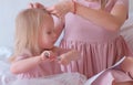 Mom braids hair to her little charming daughter in pink dresses while she painting with felt-pen. Royalty Free Stock Photo