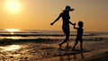 Mom and child run along the seashore against the backdrop of sunset.