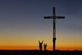 Mom with child on top of the mountain near the cross raise their arms in victory