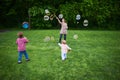 Mom and children playing soap bubbles on the green lawn in the park. Royalty Free Stock Photo