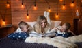 Mom with children in the winter frosty evening sitting on the bed and reading a book together. Royalty Free Stock Photo