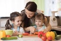 Mom chopping vegetables with kids daughters in a family home kitchen. Royalty Free Stock Photo