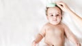 Mom is combing 6 month old toddler with baby comb. baby lies on white bed and smiles